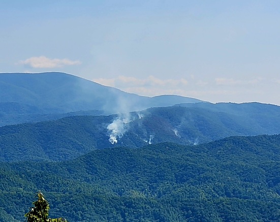 A plume of smoke rising from between rolling mountain ridges.