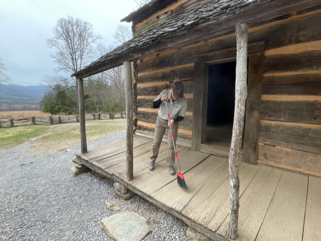 person sweeping the porch of a historic log cabin