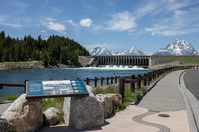 Paved pathway along river with interpretive exhibits and views of mountains