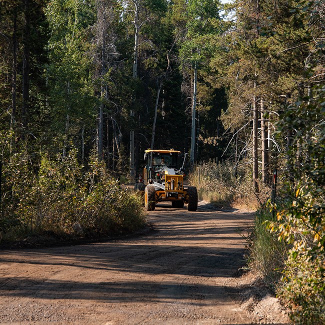 A large construction vehicle conducts work on a gravel road.