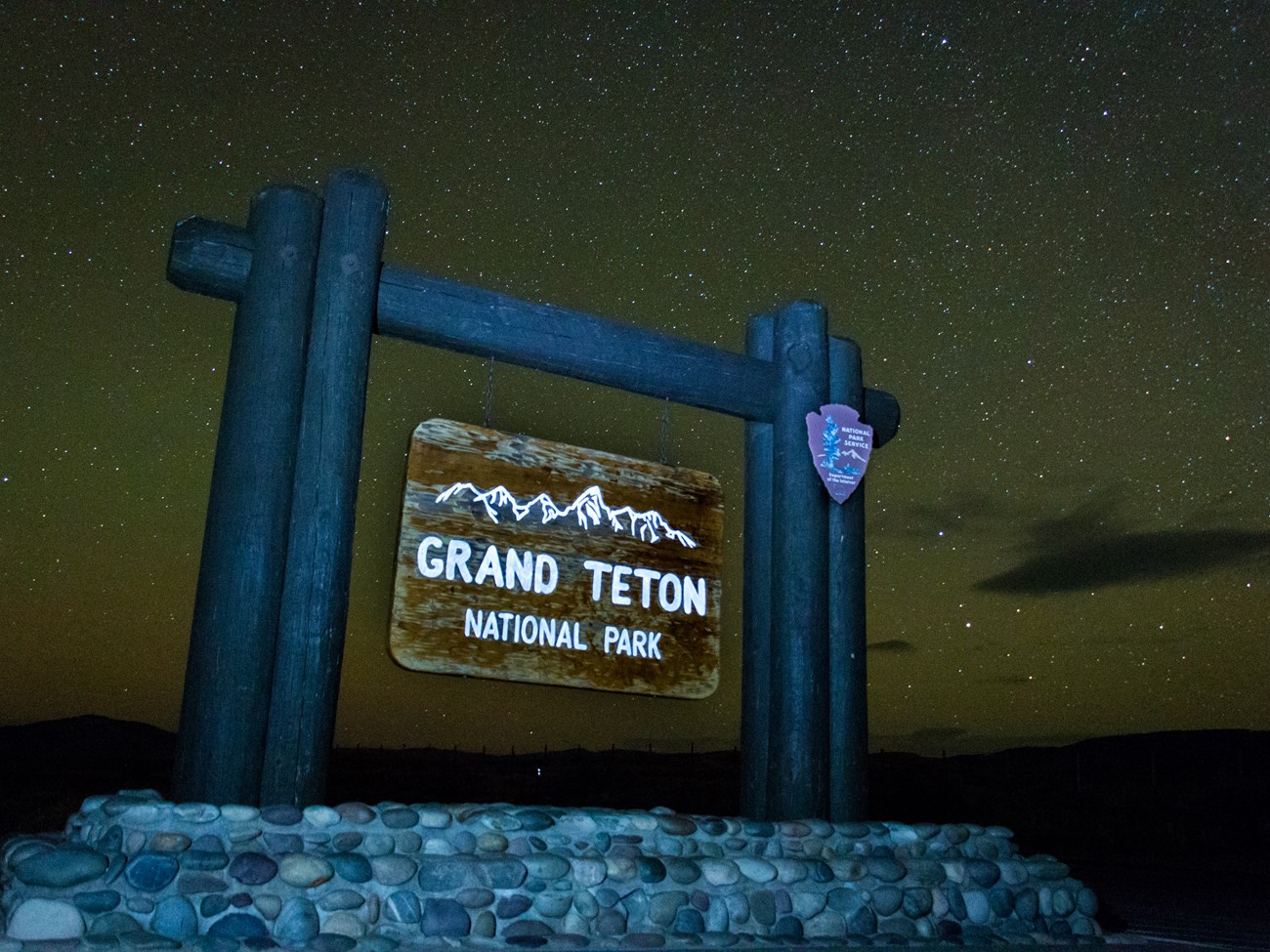 The Grand Teton Park sign stands with the stars illuminated in the background.