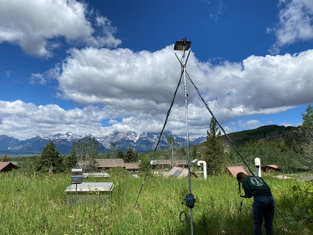 A researcher works on a luminary tripod with the Teton Range in the background