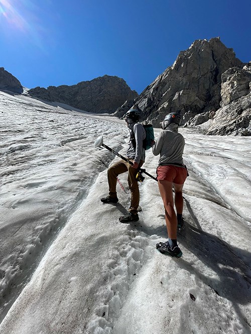 With crampons and ice axes, members of the glacier crew traverse up the steep slope of Middle Teton Glacier in the fall. The ice surace is furrowed.