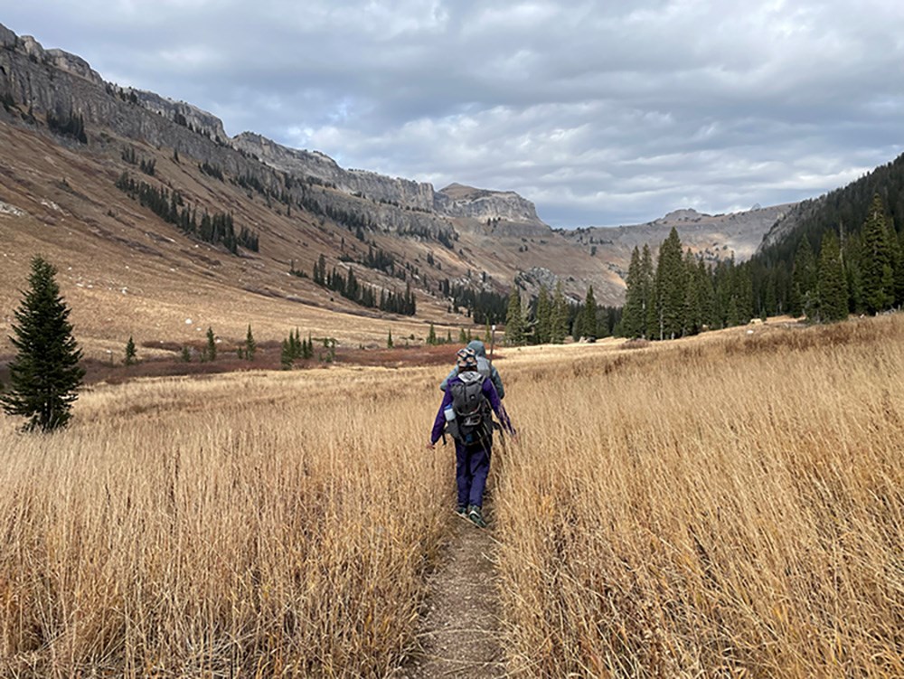 Members of the glacier crew trek down a trail thorugh a field in the fall