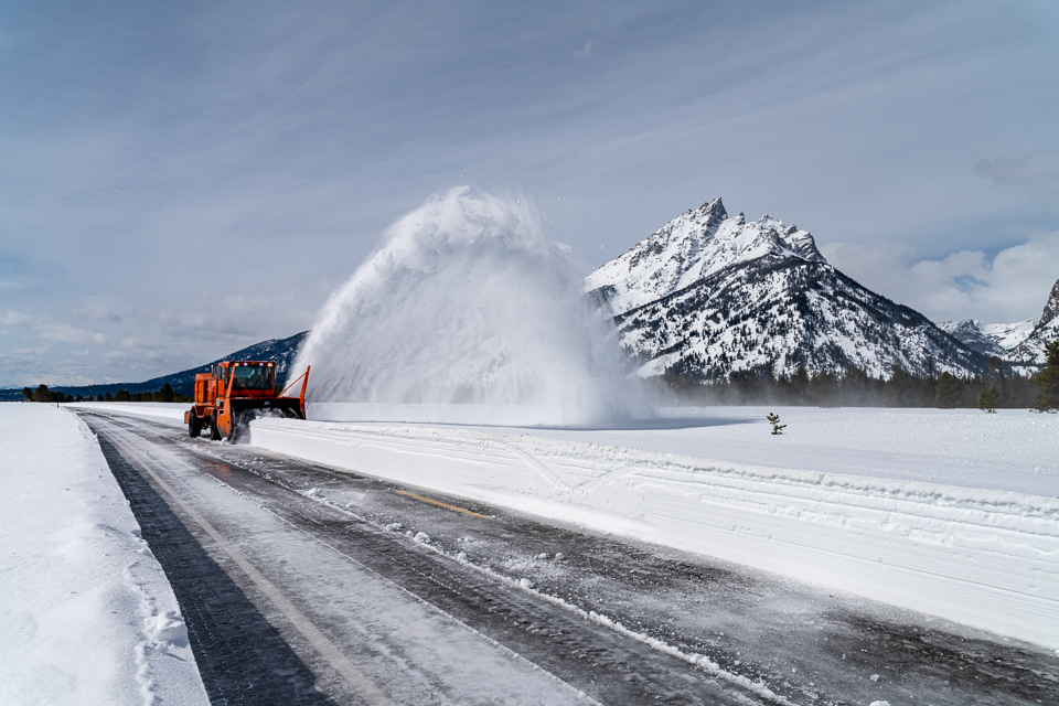 Rotary snow removal equipment removes snow from the Teton Park Road with the Teton Range in the background