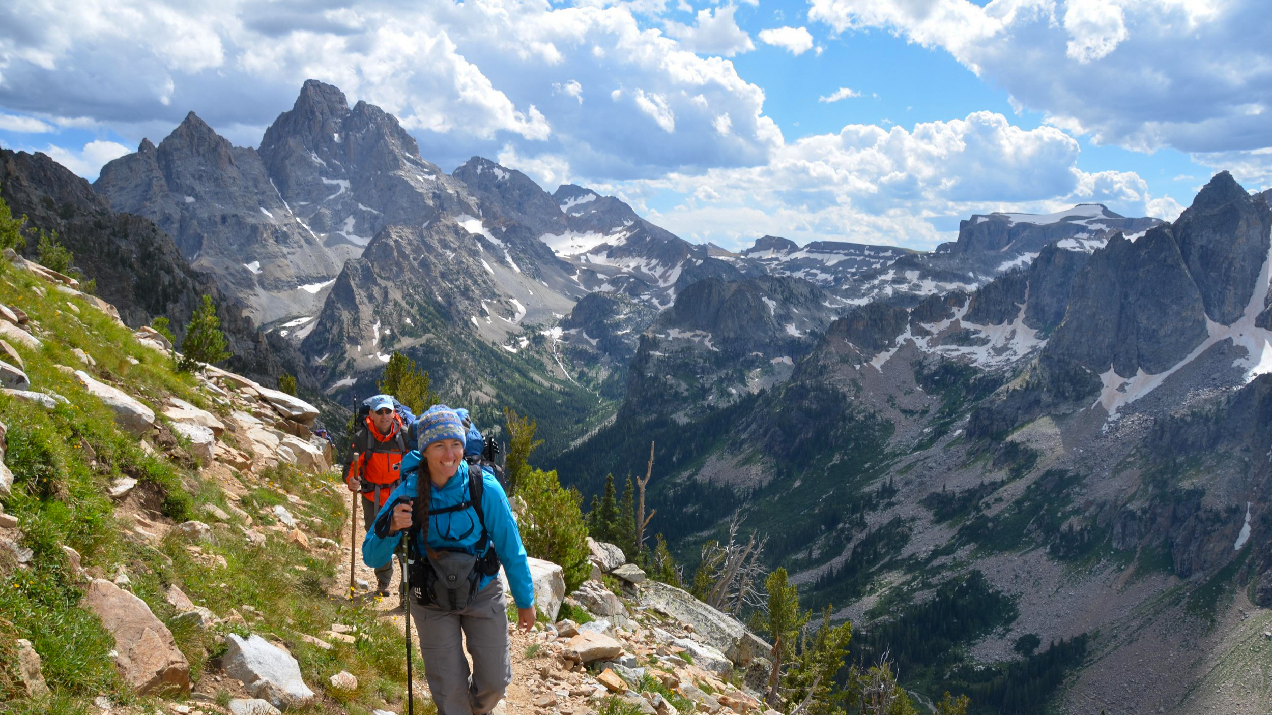 Two backcountry hikers hike up Paintbrush Divide with the Teton Range and Cascade Canyon behind