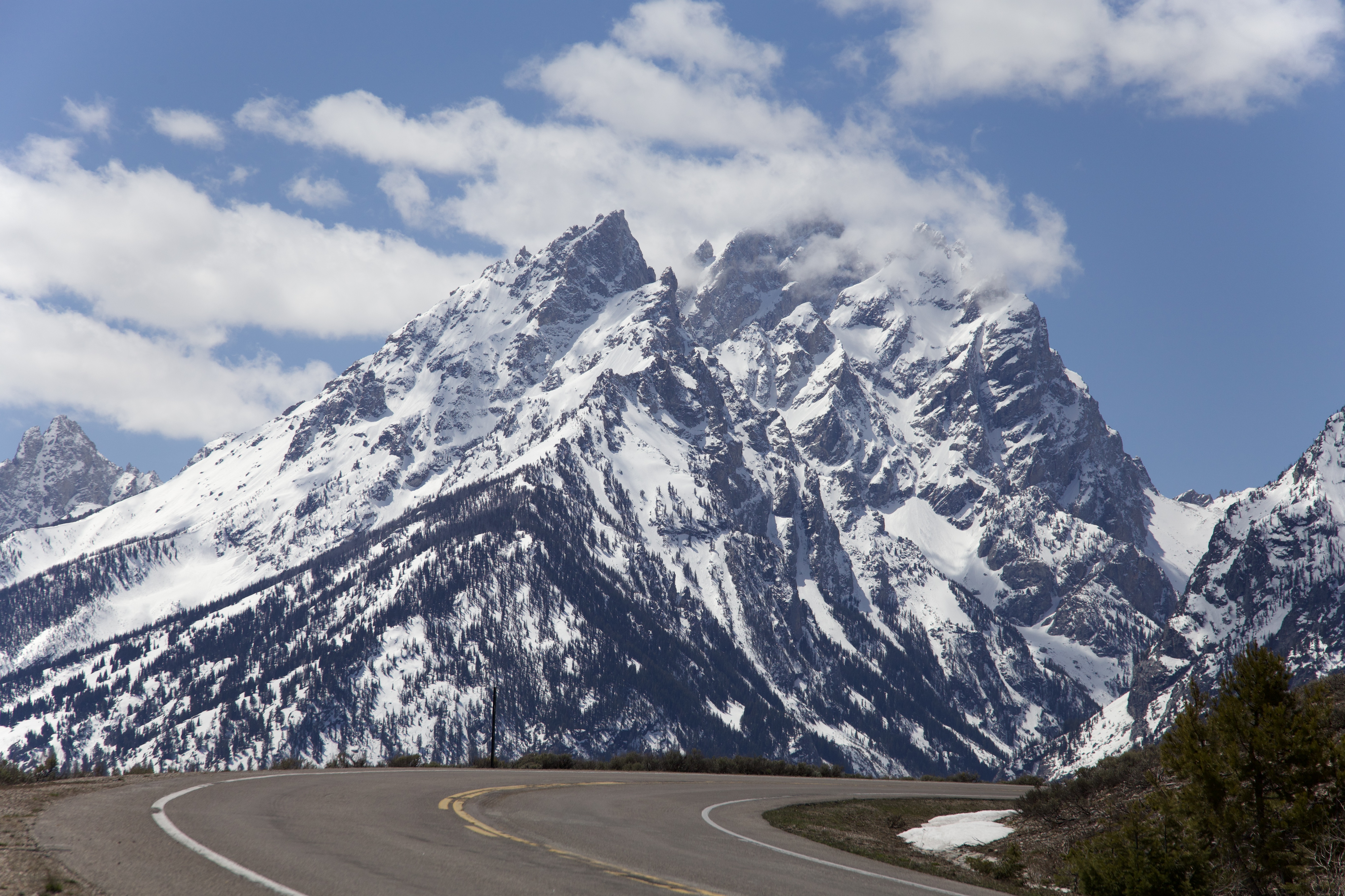 An open road winds up a hill with the Tetons in the background