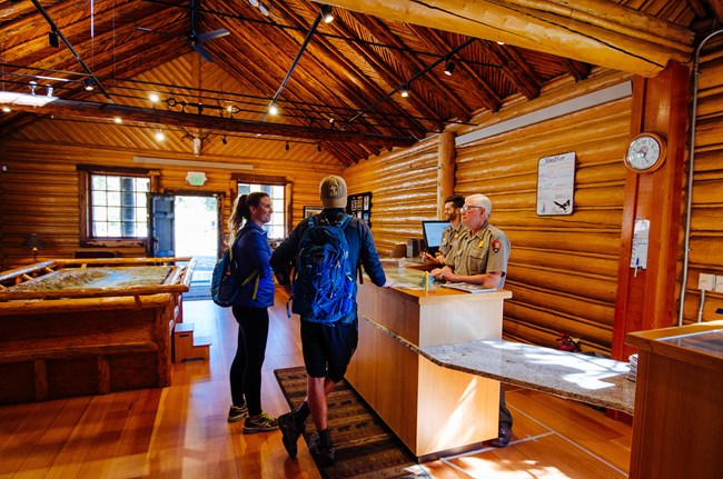 Two rangers talk to visitors from behind a desk.