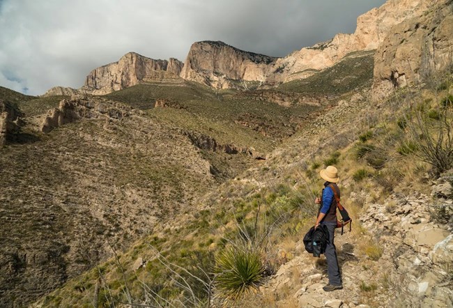 Individual stands at the base of dramatic canyon