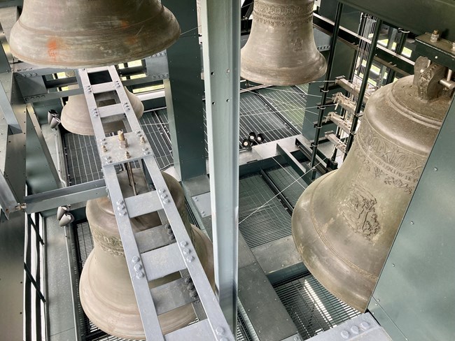 5 large bronze bells hang inside a modern steel tower