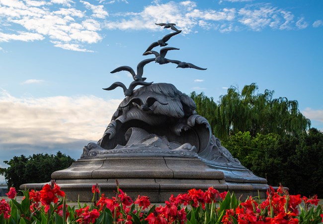 Statue of waves and seagulls surrounded by red flowers