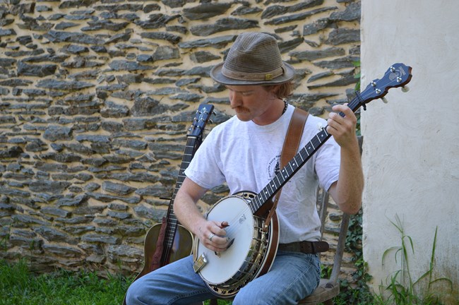 man sitting outside in front of a stone wall playing banjo