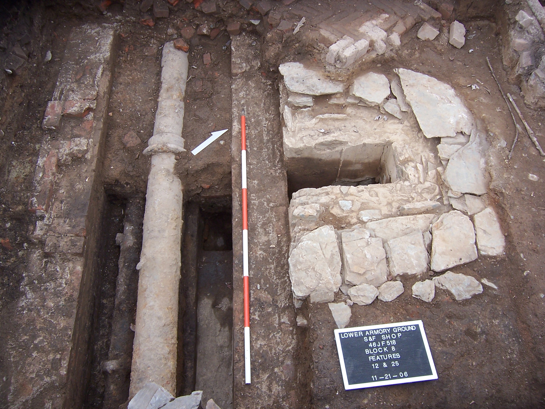 A pipe and rock foundation are exposed in an archaeological dig.