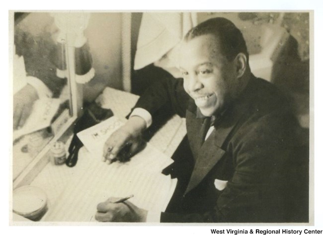 African American man sitting, smiling, with pen and paper in hand