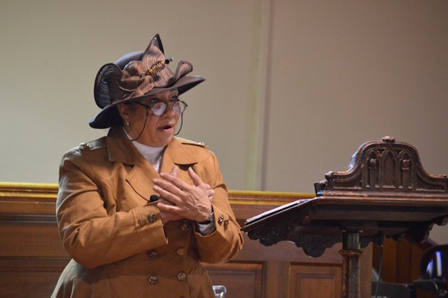 African American woman dressed in early 1900s garb; speaking at a pulpit