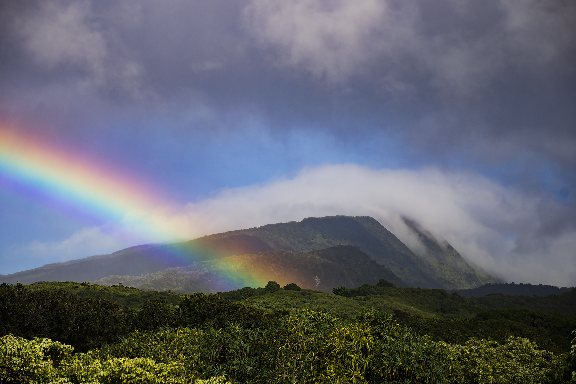 A rainbow arcs out of the verdant Kīpahulu Valley as clouds descend from the top of the ridge.