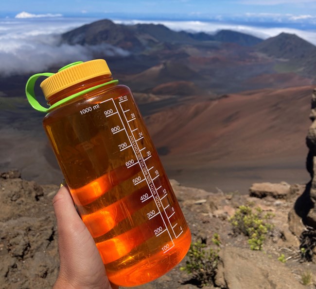 An orange water bottle outside with the crater in the background.