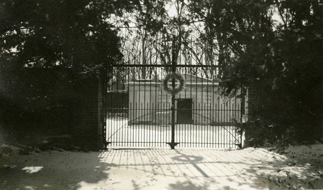 a black and white photograph of the cemetery gates in the snow