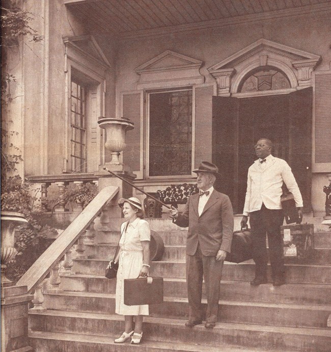 Black and white photograph of John Ridgely Jr. and his wife Jane with a black servant carrying their bags on the front porch of the Hampton mansion.