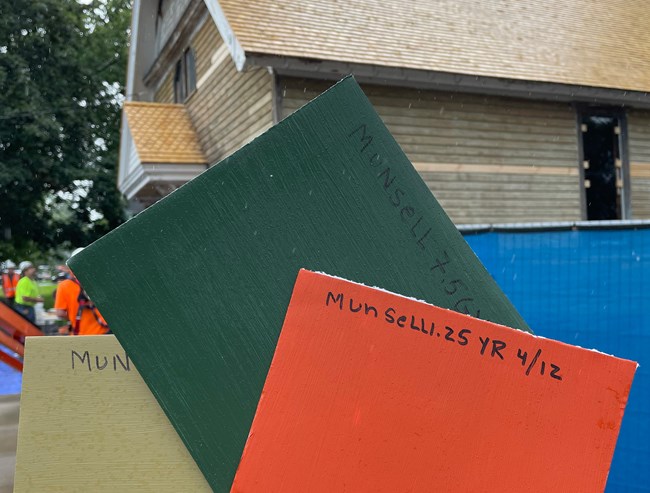 A hand holding up colored paint swatche sin front of a church building