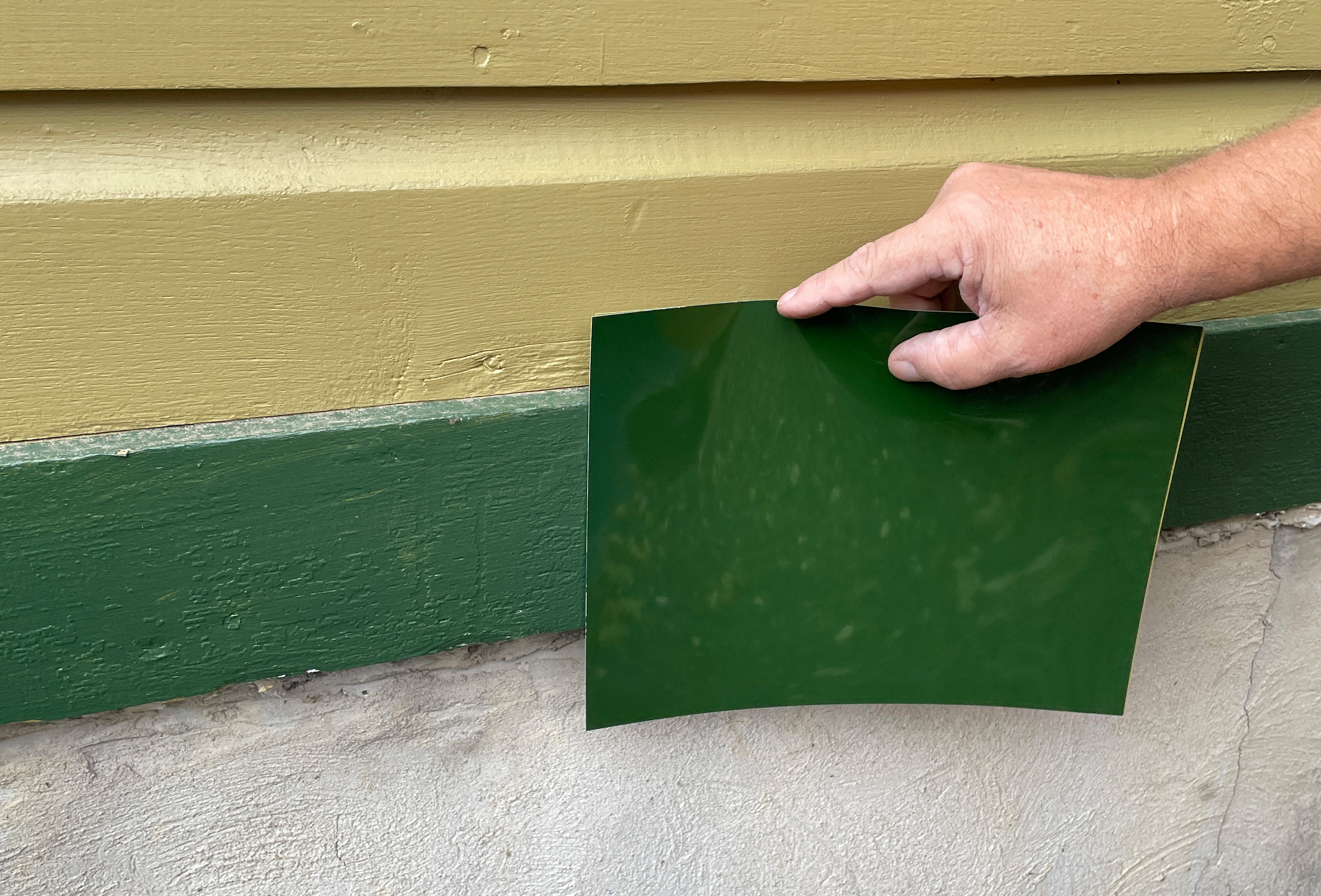 A green colored plastic sheet held up against green trim. There is a slight difference in the color.