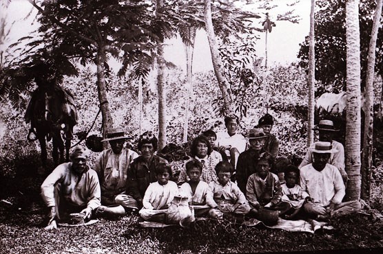 Black and white portrait of a Hawaiian family in 1890s garb sitting on the side of a road