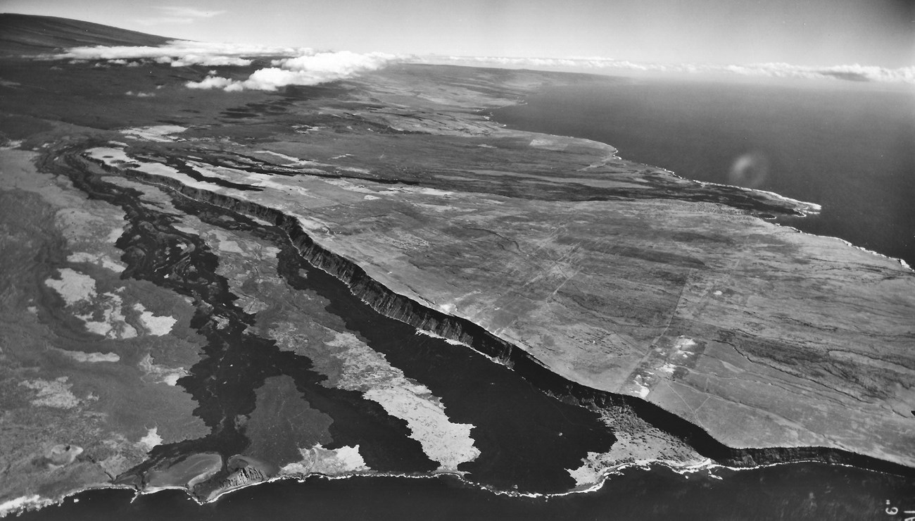 Black and white aerial view of lava flows leading from an island into the sea