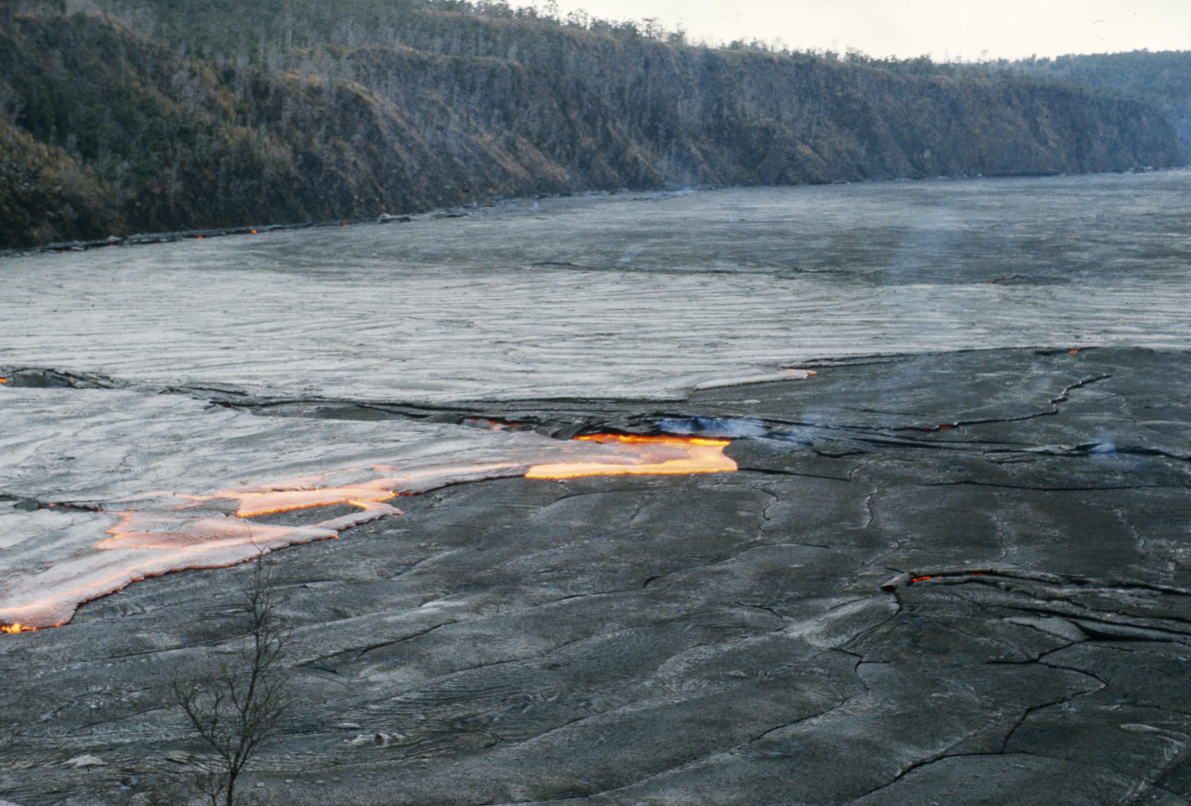 Glowing orange molten lava flow on the floor of a caldera with forested walls