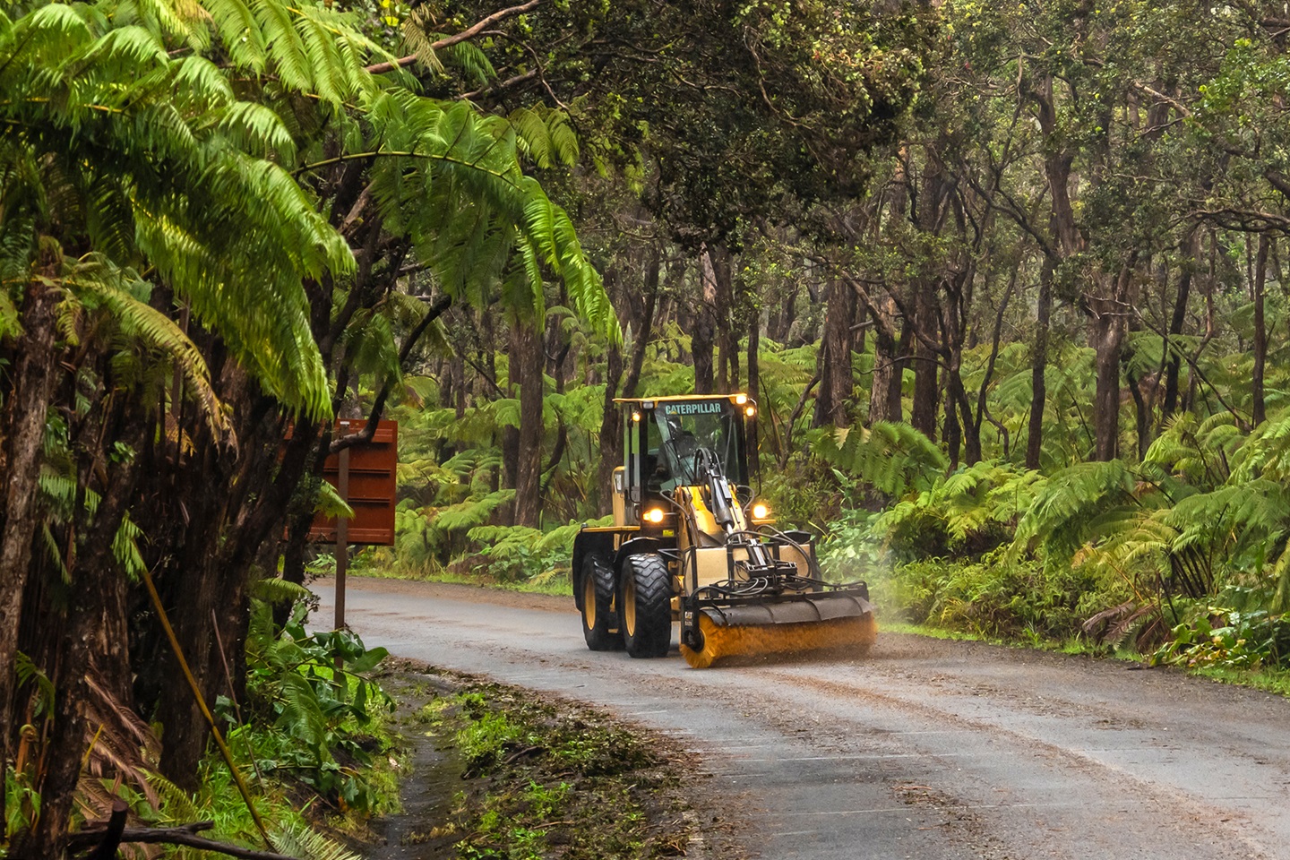 A street sweeper cleans a two lane forested road