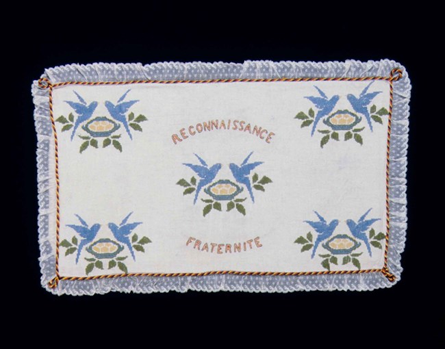 Embroidered cloth from a flour sack depicts blue birds with the words Reconnaisance and Fraternite.