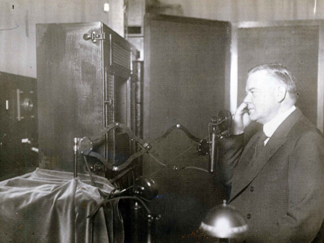 A man speaking by phone in front of a primitive television camera in 1927.