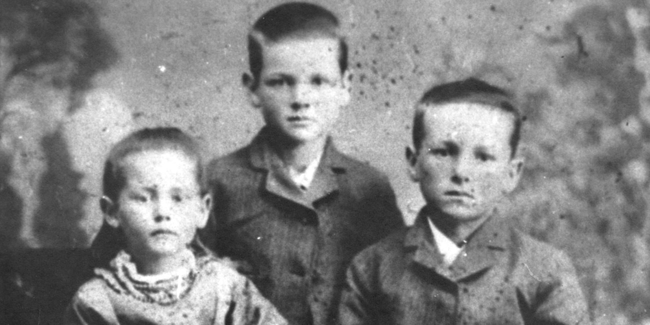 An eight year old boy poses for a portrait in 1881 with his younger sister and older brother.