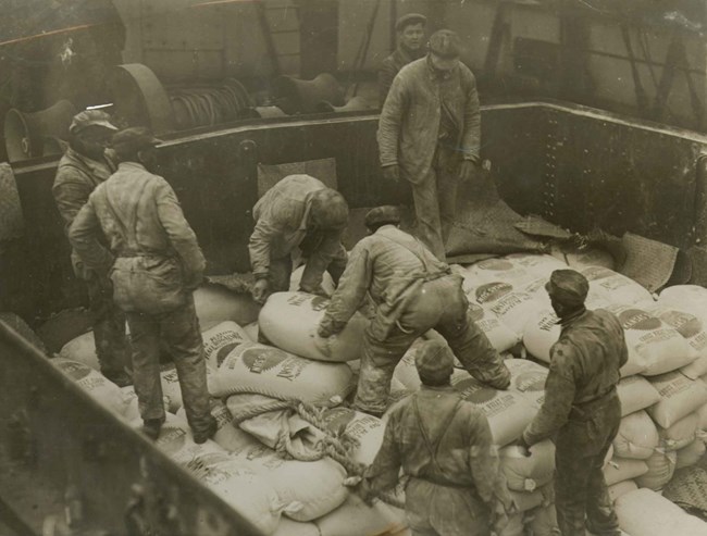 Workmen load a ship with sacks of donated flour.