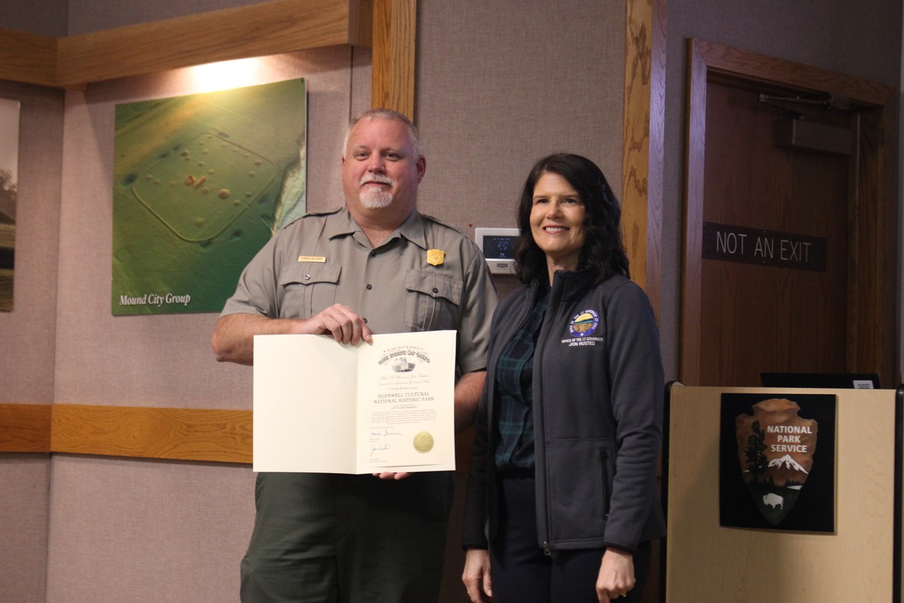 a uniformed ranger holds a certificate and poses with a female dignitary.