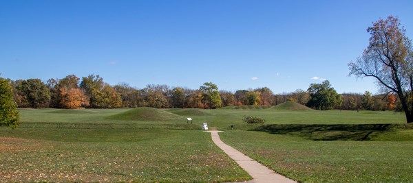 Green grass-covered mounds and colorful trees in the background under a deep blue sky