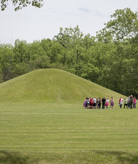 Kids walk in front of a large mound in a grassy field
