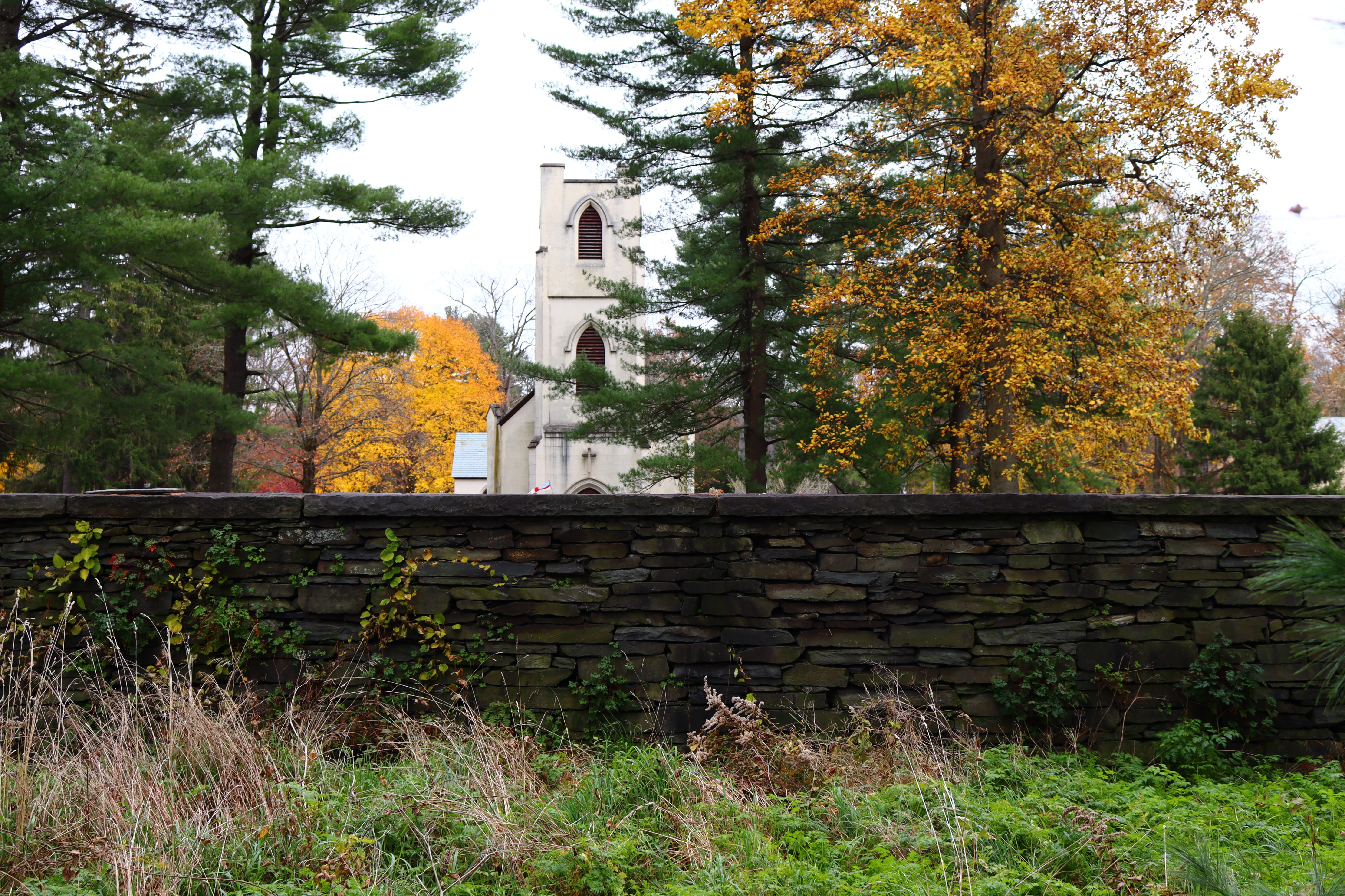 A stone wall with a church and trees behind it