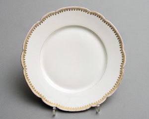A white china dinner plate with scalloped and gilt edge.