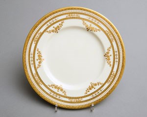 A white porcelain plate with gilt decorated rim of narrow bands and garlands.