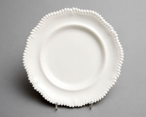 White porcelain dinner plate with raised scalloped edge.