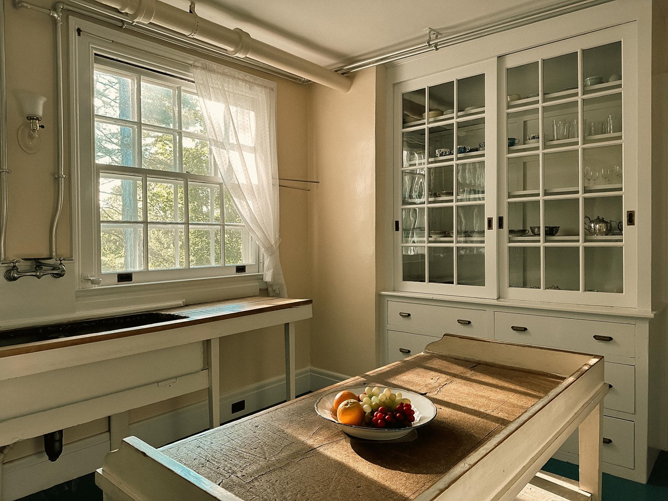 A room with sink under a window and built in cupboards along the wall.