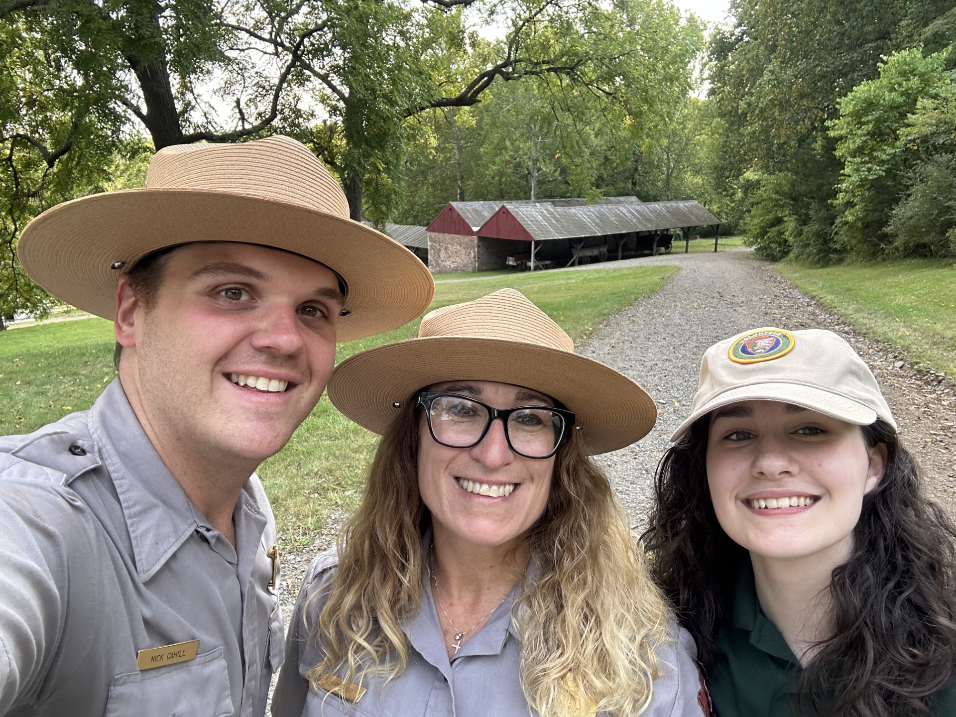 Three people smile at the camera. Two wear national park service uniforms and the other wears a volunteer uniform hat.
