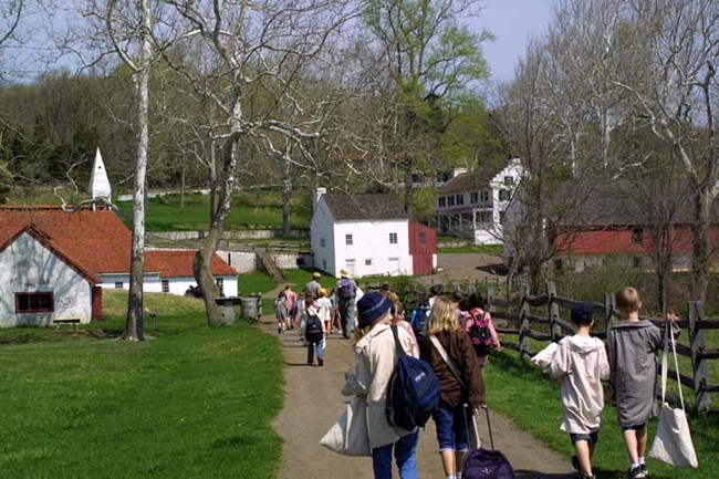 Students walk to the Barn. Cast House, Blacksmith Shop, Ironmaster's Mansion, Office/Store and Barn are in view.