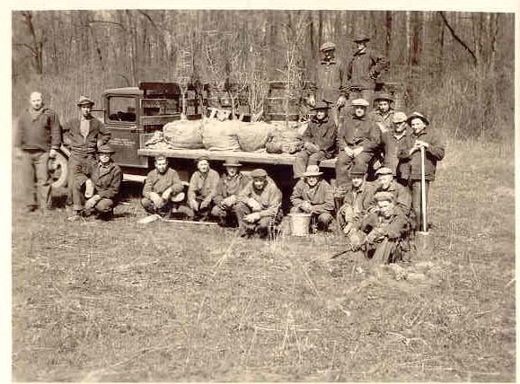 Group of CCC members posing for a picture in front of a truck with supplies to plant trees. Supplies include shovels, buckets and trees.