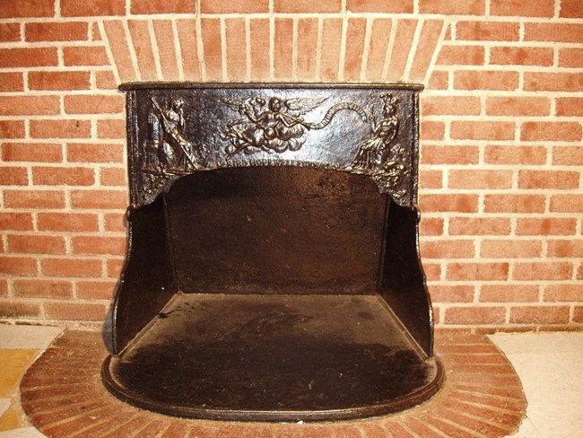 Franklin Stove inserted into a red brick wall. The stove is ornate and contains the words "Hopewell Furnace".