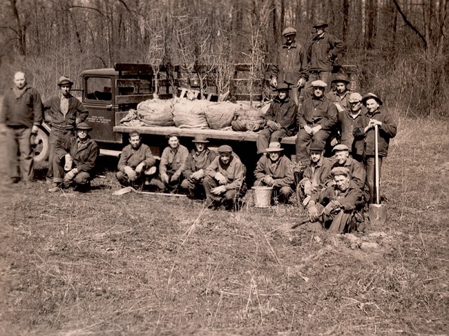 A group of people in work close pose around a truck full of small trees ready to plant them.