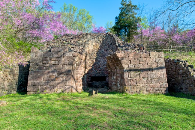 Exposed stone furnace stack surround by grass and trees.