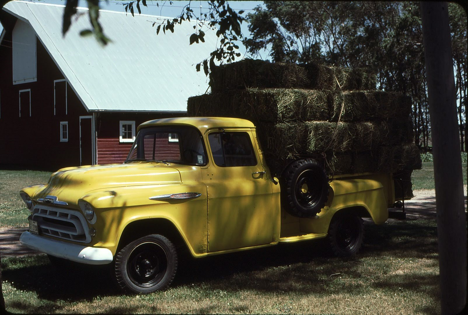 Yellow truck with a load of hay parked near a barn.