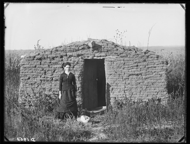 Woman standing in front of a sod house