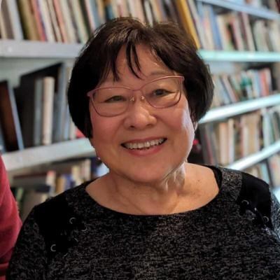 An Asian woman in glasses smiling in front of bookshelves